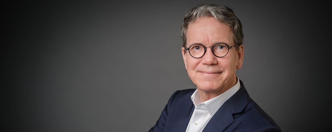 Mann l&auml;chelt mit verschr&auml;nkten Armen in die Kamera