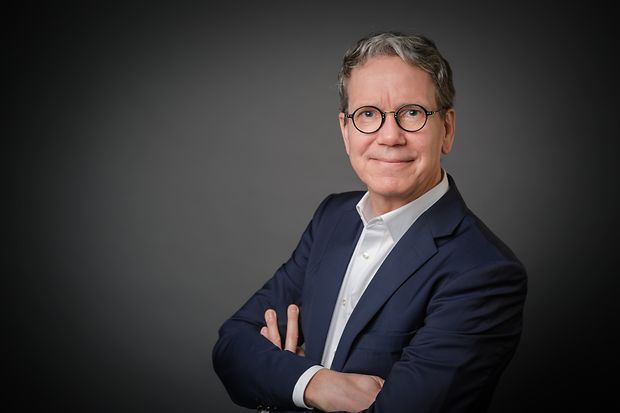 Mann l&auml;chelt mit verschr&auml;nkten Armen in die Kamera