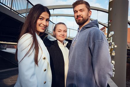 Zwei junge Frauen und ein junger Mann schauen in die Kamera.