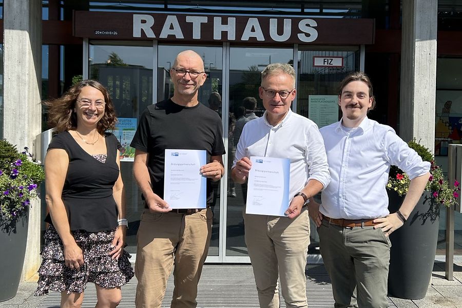 Vier Personen stehen vor dem Rathaus und schauen in die Kamera.