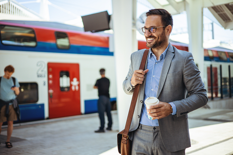 L&auml;chelnder Gesch&auml;ftsmann am Bahnsteig mit Coffe-to-go in der Hand.