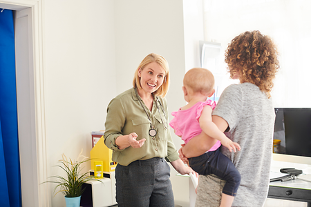 eine Frau stehend und eine Frau mit Baby auf dem Arm an Arbeitsplatz