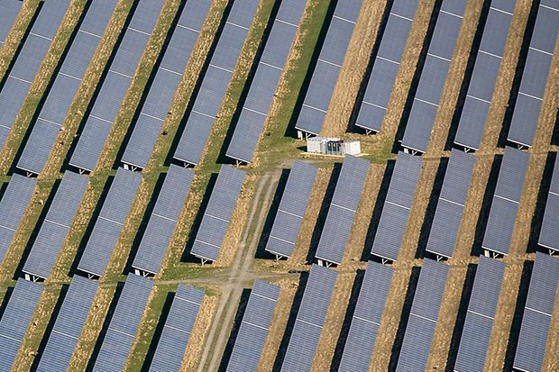 Luftaufnahme eines Solarparks mit langen Reihen von Solarmodulen auf einer Freifl&auml;che.
