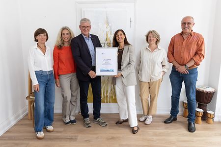 Vier Frauen und zwei M&auml;nner stehen f&uuml;r ein Foto zusammen und halten eine Urkunde