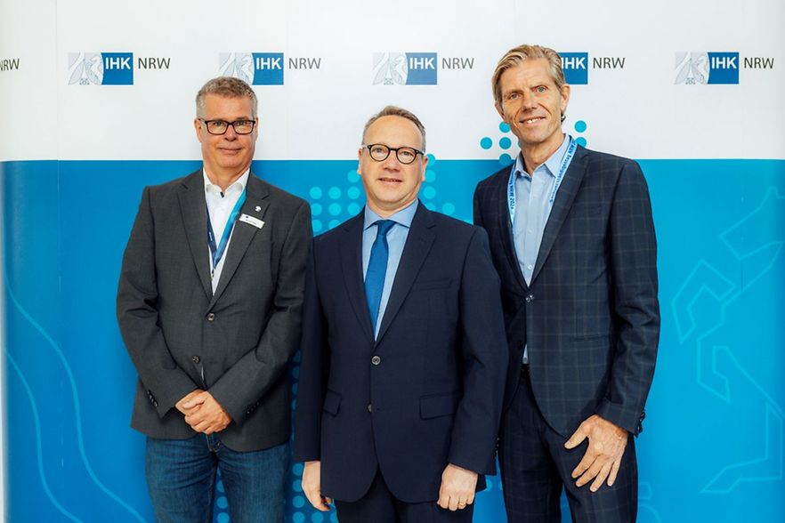 Drei M&auml;nner beim Sachverst&auml;ndigentag NRW 2026 vor einer IHK-NRW-Wand