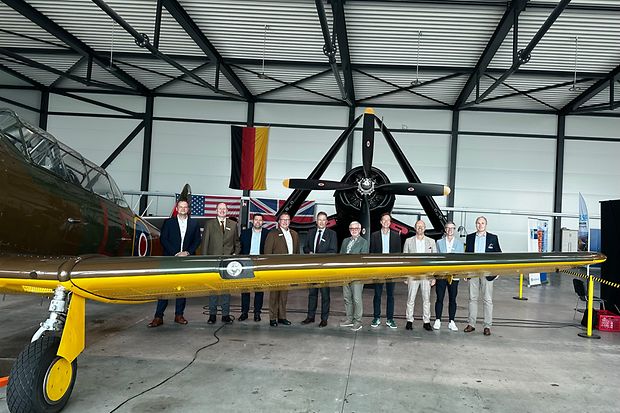Eine Gruppe von Personen steht hinter der Tragfläche eines kleinen Flugzeugs.