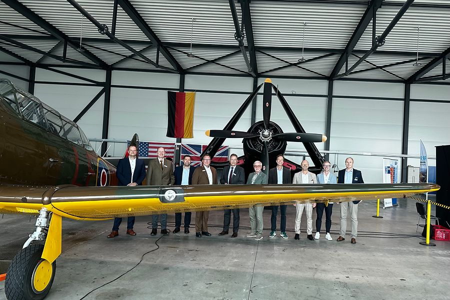 Eine Gruppe von Personen steht hinter der Tragfläche eines kleinen Flugzeugs.